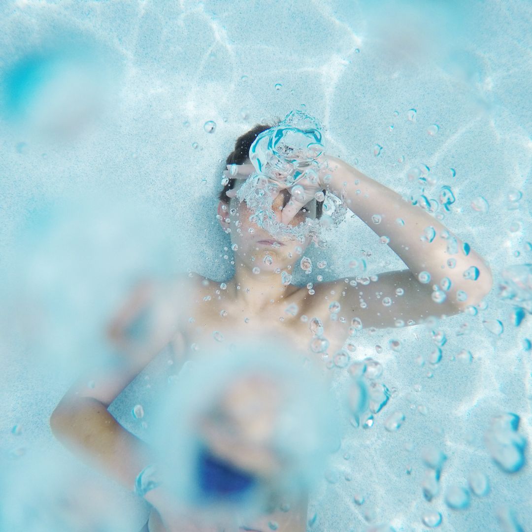 A boy blowing bubbles while in a pool